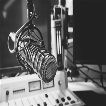 A black and white photo of a microphone in front of a radio, illustrating contact information for Orb Music Studio.