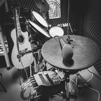 A black and white photo of a drum set in Orb Music Studio's recording studio, professionally engineered.