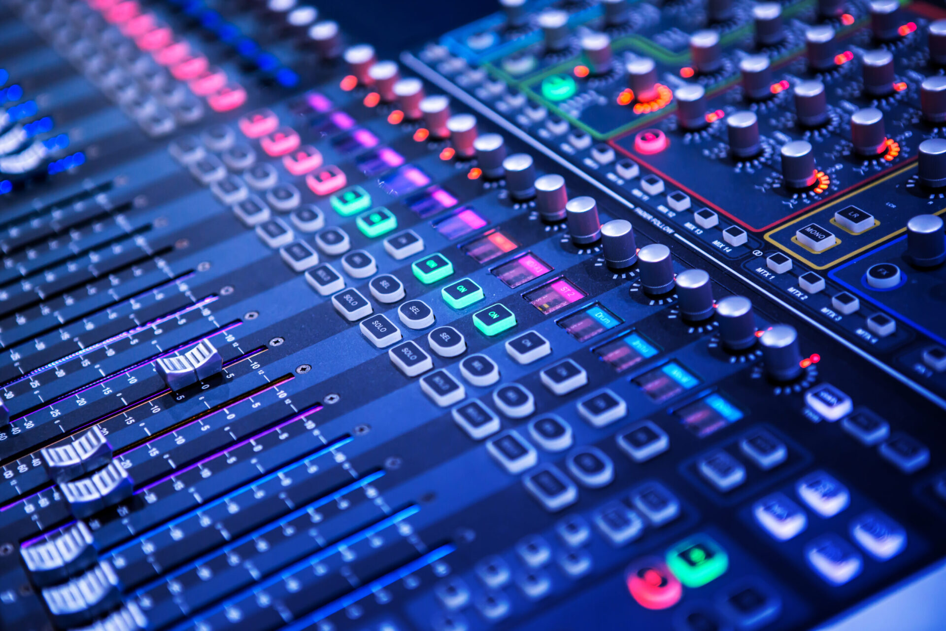 A close up of an engineer working on a mixing board with colorful lights.